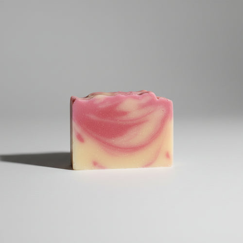 A rectangular bar of handmade soap with a pink and pale yellow marbled swirl pattern, resting on a textured gray fabric background.
