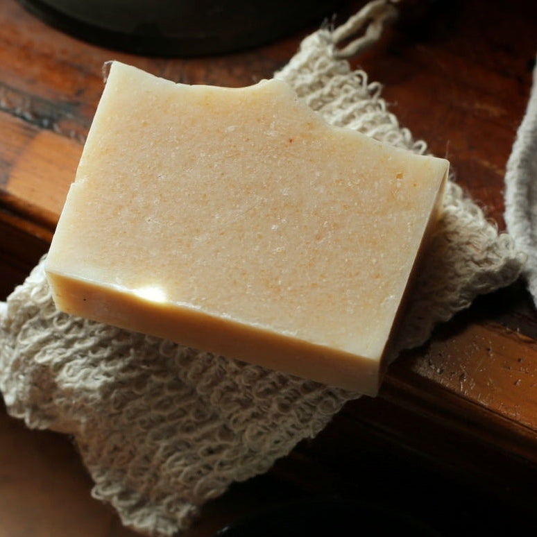 A rectangular bar of pale beige soap resting on a textured off-white cloth over a dark wooden surface.